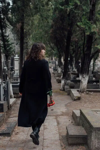 Girl on black coat in graveyard with red flowers