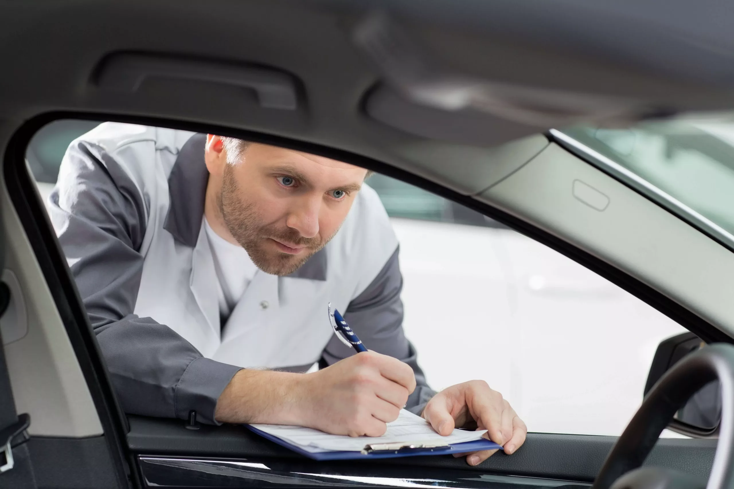Bodyshop employee examining car taking notes on a clipboard scaled