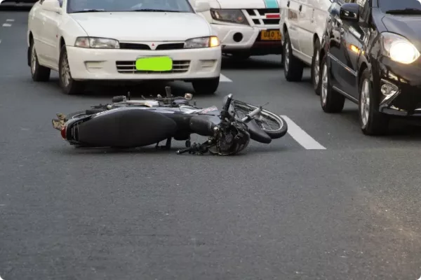 motorcycle laying on road in front of white car after motorcycle accident