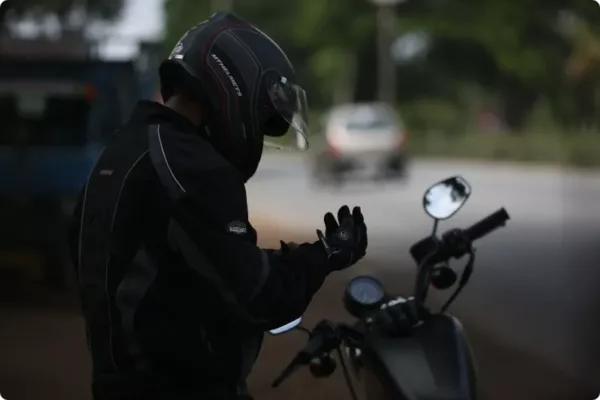 biker with black gear, wearing black motorcycle helmet putting on gloves looking down